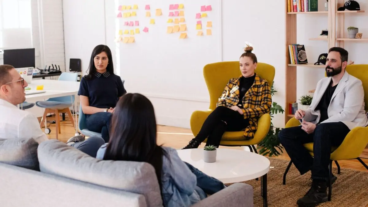 Ein Team sitzt im Kreis in einem modernen Raum mit einem Kanban-Bord im Hintergrund