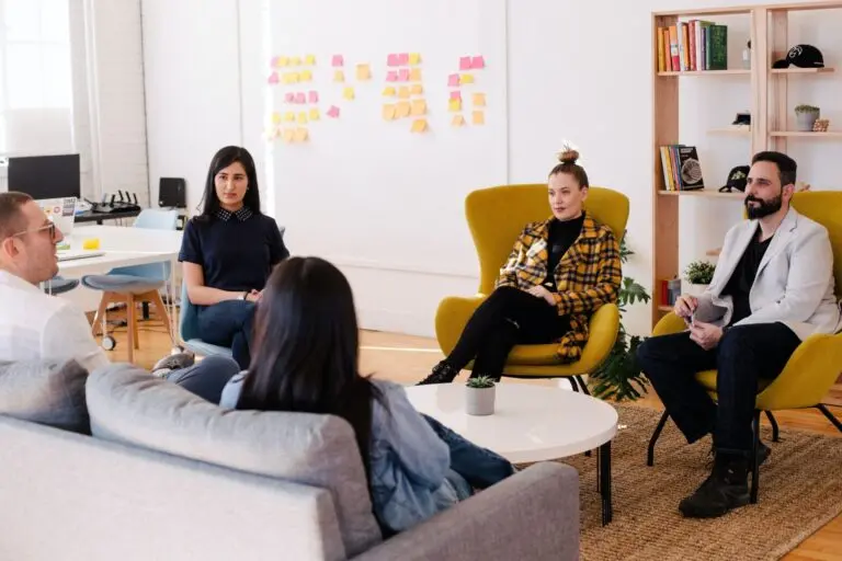 Ein Team sitzt im Kreis in einem modernen Raum mit einem Kanban-Bord im Hintergrund