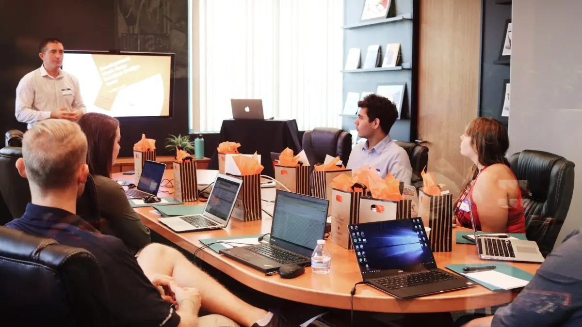 Mann steht vor Menschen, die neben einem Tisch mit Laptops sitzen