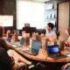 Mann steht vor Menschen, die neben einem Tisch mit Laptops sitzen