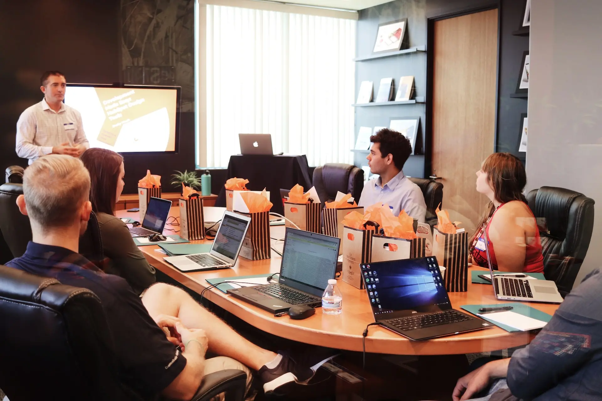 Mann steht vor Menschen, die neben einem Tisch mit Laptops sitzen