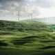 Windräder auf einer grünen Wiese vor Bergen